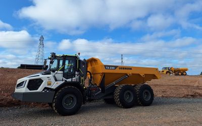 An SER Liebherr TA230 dump truck with distinctive white cab and a Volvo A30G dump truck parked under a blue sky.